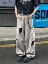 Men’s light gray distressed denim wide leg jeans with black patchwork repairs and a chain belt plus size