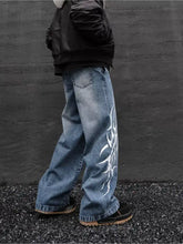 Men’s blue denim wide leg jeans with bold white tribal-style graphic on outer leg made from durable fabric blend
