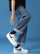 White nike air force 1 sneakers with black swooshes and laces paired with men’s relaxed fit cuffed hem jeans