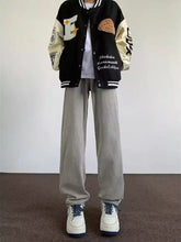 Men’s full size wash wide leg jeans paired with a black and cream varsity jacket with embroidered patches and contrasting sleeves