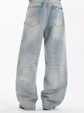 Men’s light-wash size wide leg jeans with frayed hems and silver chains with green beads on back pockets