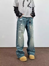 Men’s full size wide leg blue denim jeans with distressed finish and unique white and black paint splatter accents