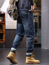 Men’s plus size dark-wash denim relaxed fit jeans with drawstring waist and rolled cuffs paired with tan work boots