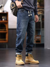 Men’s plus size dark-wash denim relaxed fit jeans with drawstring waist and rolled cuffs paired with tan work boots