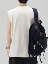 Black canvas backpack with brown leather accents and silver zipper pulls shown alongside a men’s plus size round neck tank