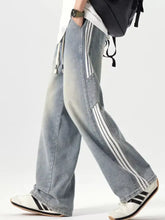 Men’s plus size washed wide leg jeans in light wash denim with three white side stripes paired with adidas sneakers