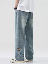 Men’s plus size light-wash denim relaxed fit jeans with a wide leg cut and guns patch on the lower left leg