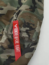 Red remove before flight tag with white lettering attached to zipper of men plus size camouflage bomber jacket