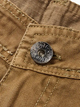 Close-up of tan cotton fabric with stitching and embossed metal button on mens pocketed pants