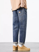 Men’s straight fit wash jeans in blue denim with relaxed fit, rolled cuffs, and brown leather patch on the back pocket