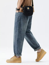 Black Carhartt crossbody bag with yellow logo patch paired with men’s relaxed fit jeans for casual use