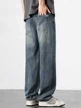 Men’s wash relaxed fit jeans in faded blue denim with wide-leg cut, subtle whiskering, and detailed stitching