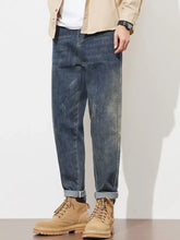 Men’s washed loose fit dark-wash denim jeans with subtle fading, distressed details, relaxed fit, and rolled cuffs
