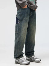 Dark-wash men’s relaxed fit jeans with a navy patch featuring a white number 6 on the thigh