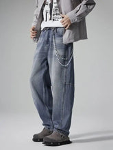 Men’s washed relaxed wide-leg jeans in faded blue denim with visible stitching and a chain accessory across the front