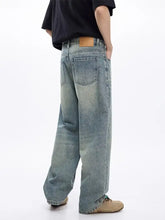 Men’s washed wide leg jeans in light-wash denim with a wide-leg cut and tan leather back pocket tab shown from back side