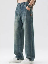 Men’s washed wide leg relaxed fit jeans in faded blue denim with subtle whiskering and brown leather side patch