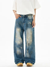 Men’s wide leg denim jeans in faded blue wash with distressed paint-splatter gold accents