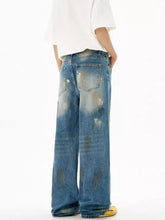 Men’s wide leg jeans in faded blue denim with intentional distressing and classic back pockets shown from the back side