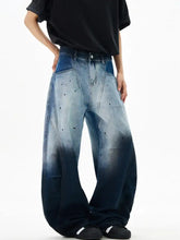 Mens wide leg denim pants with gradient fade light blue to dark indigo, distressed black speckles, and raw hem detailing