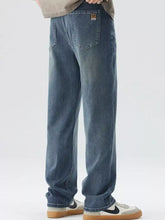 Men’s wide leg blue denim jeans with faded wash and small brown patch on the back pocket shown from the back side