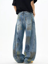 Men’s wide leg denim jeans with faded blue wash and abstract greenish-yellow paint splatter pattern
