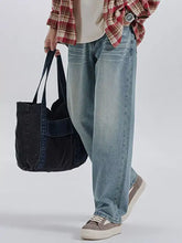 A black denim tote bag with sturdy handles and a patch pocket for men complementing wide leg washed jeans