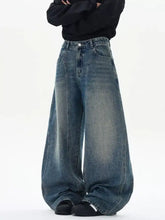 Men’s wide leg washed jeans in faded medium blue denim with subtle whiskering and raw hem detailing