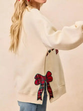Back of cream-colored merry bow slit crew neck christmas sweatshirt with red and green plaid bow appliqué made of slightly stretchy material ideal for machine wash cold care