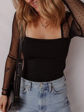 Black leather crossbody bag with sleek minimalist design and buckle detail complementing mesh sleeve square neck bodysuit