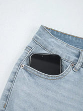 A black smartphone in the front pocket of light-wash mid rise ankle-length distressed skinny jeans with slight stretch