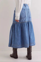 Back view of a medium-wash midi denim skirt with a tiered flared silhouette and two back pockets