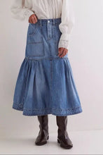A mid-blue midi denim skirt with two front patch pockets and a tiered flared hem in denim fabric