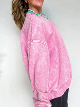 Pink mineral wash cotton sweatshirt with subtle faded patterns and white stitching details, machine wash care instructions