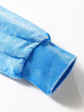 Blue mineral wash sweatshirt sleeve with ribbed cuffs showing care instructions for machine wash durability