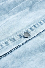 A silver-toned button on light-wash denim fabric of a mineral wash ruffle sleeve denim dress with visible stitching