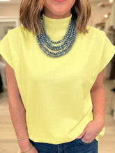 A layered necklace with gray faceted beads paired with a mock neck cap sleeve blouse in a classic style