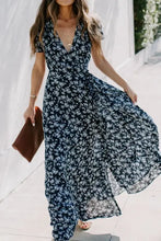 Woman in navy blue floral surplice short sleeve maxi dress with clutch