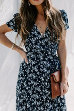 Woman in navy blue floral surplice short sleeve maxi dress with clutch