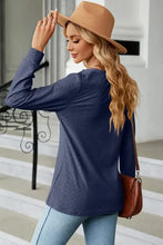 Woman in notched long sleeve t-shirt, navy blue top, light blue jeans, holding brown hat