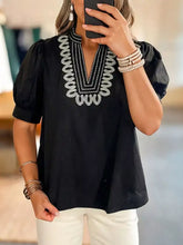 Black short-sleeved puff sleeve blouse with notched puff sleeves and intricate white beaded embroidery on v-neckline