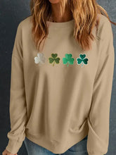 Beige long-sleeved sweatshirt with green shamrock designs, fuzzy trim, and metallic accents
