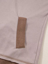 A beige woven waffle patchwork exposed seam patch sewn on the side of a light gray oversize casual hoodie