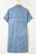 A light blue oversized button down denim shirt dress with short sleeves and collar hanging on wooden hanger