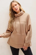 Woman in oversized tan drawstring turtleneck long sleeve sweatshirt
