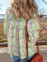 A woman wearing a light green paisley print half puff sleeve blouse with purple and beige patterns and a relaxed fit