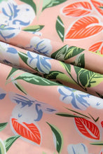 Pastel floral print summer dress with peach fabric, leaves, orange flowers, white blossoms on pink background