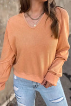Woman in peach V-neck long sleeve waffle knit top, ribbed cuffs, jeans