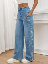Light-wash denim pearl embellished wide leg jeans with a vertical row of white pearls along the outer seam