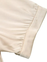 Cream-colored pearl trim satin bodysuit sleeve with smooth reflective finish and neatly stitched hem detail